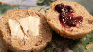 A split roll with butter on one half and red fruit jam on the other, placed on a colorful plate.