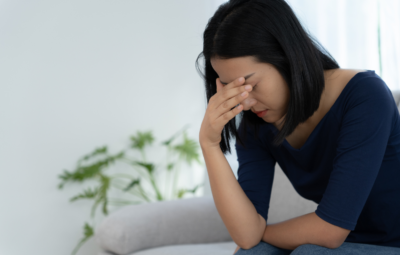 A woman sitting on a sofa with her hand on her forehead, looking stressed.