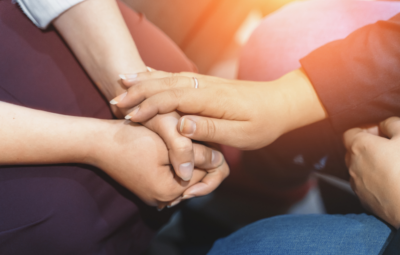 Two pairs of hands gently holding each other, symbolizing support and comfort.