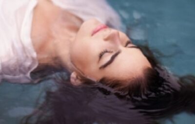 A person with closed eyes floats peacefully in clear water, wearing a white garment.