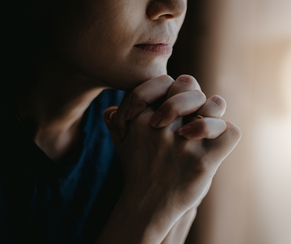 Person in thoughtful pose with hands clasped, close-up on face and hands in soft lighting.