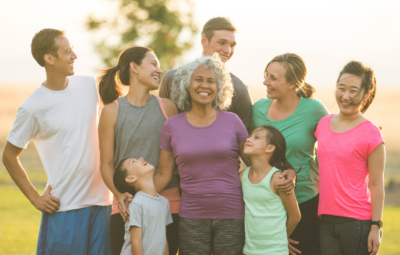 A diverse, happy group of people standing outdoors, smiling and embracing each other in a park setting.