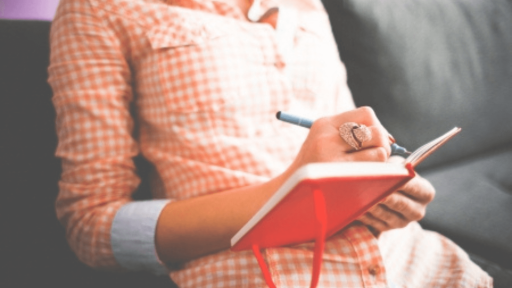 Close up on a person's torso as they write in a red notebook