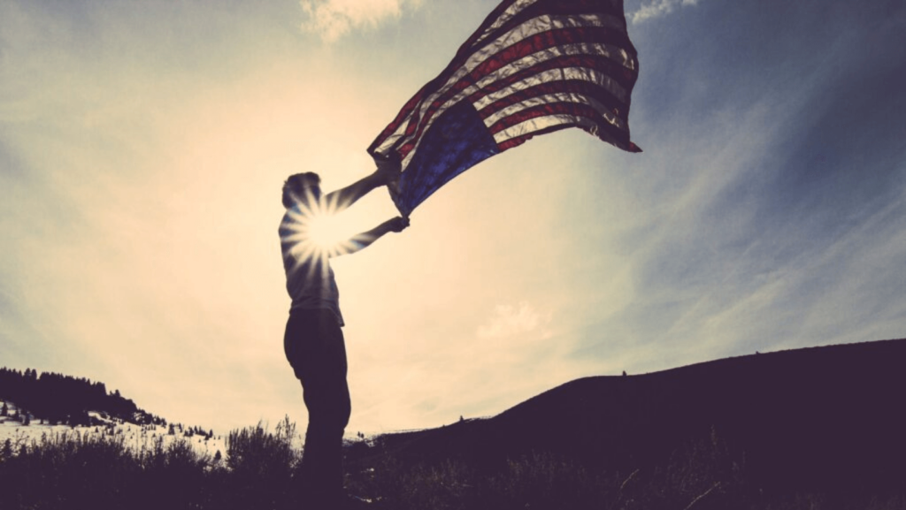 Person outdoors silhouetted against the sky holding an American flag