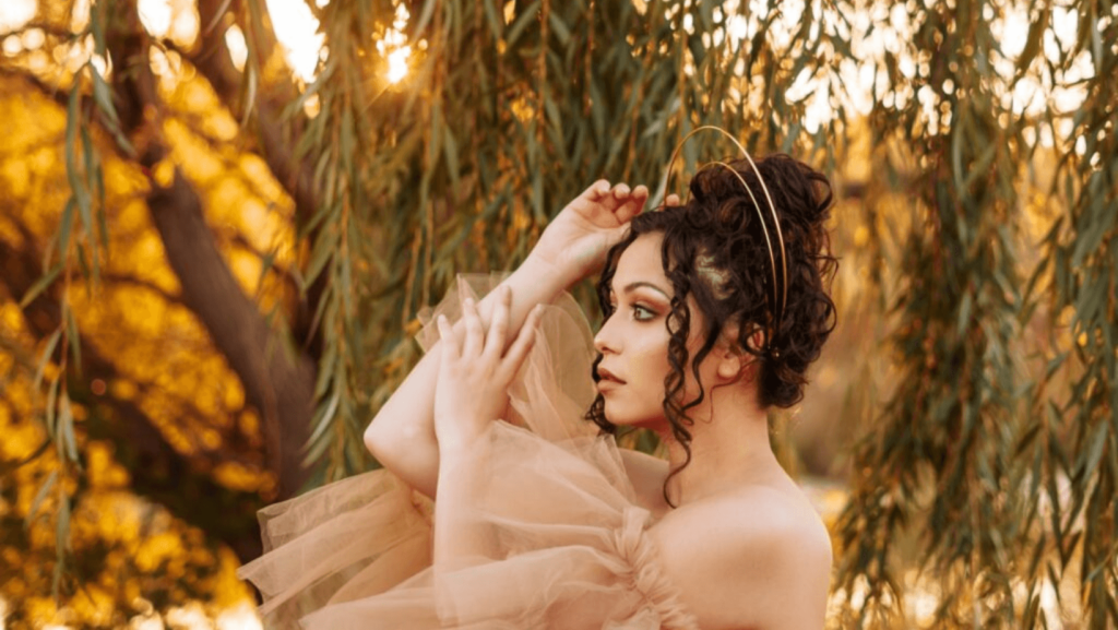 Woman with dark hair in profile, wearing a tulle dress, outside in front of trees