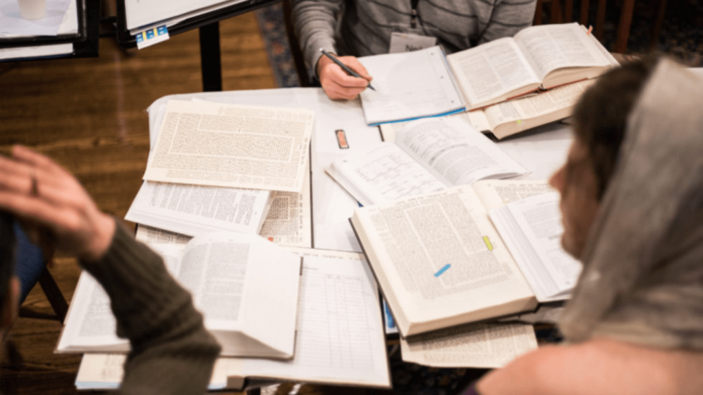 People sitting around a table piled with open prayer books