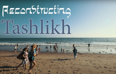 People walking on a beach during the day with Reconstructing Tashlikh text overlay.