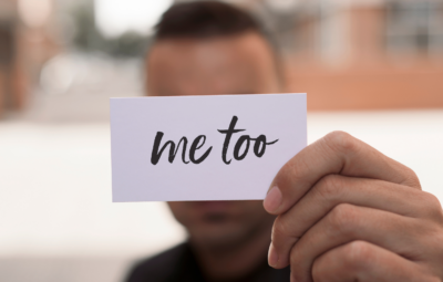 Person holding a card with me too written on it, background blurred.