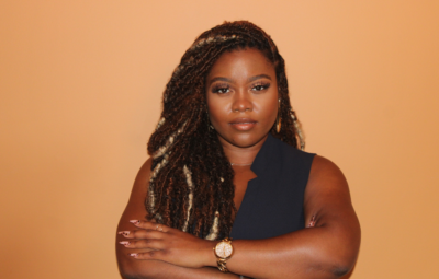 Person with braided hair and a watch, crossing their arms, against a peach background.