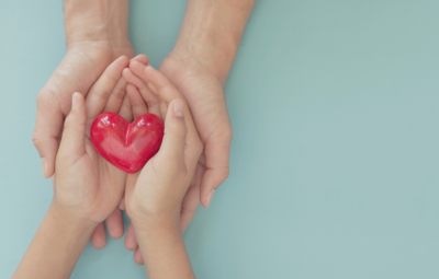 Adult and child hands holding a red heart shape against a light blue background.