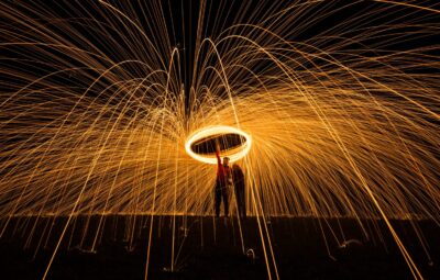 A person spins a ring of sparking lights at night, creating swirling patterns of bright orange trails in the dark sky.