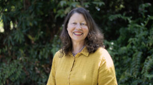 A waist-up image of Gabrielle Kaplan-Mayer, standing in front of a tree.