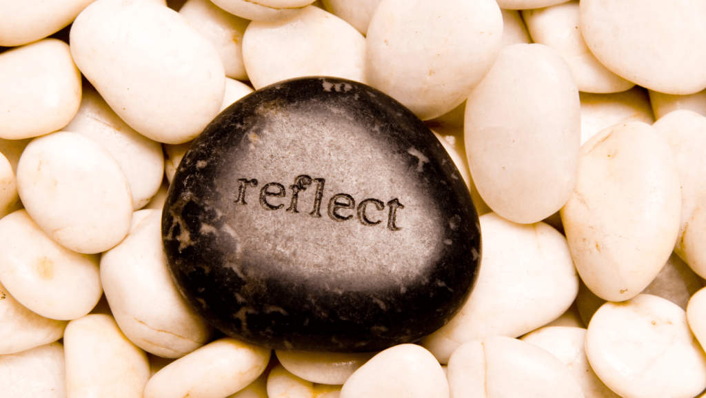 A black stone engraved with the word Reflect on a collection of white stones