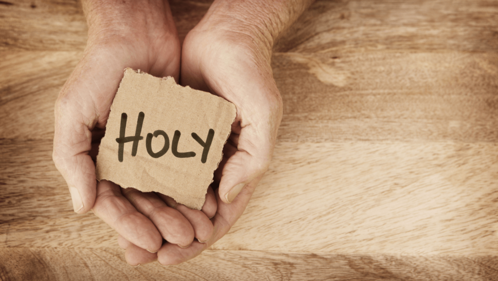 A person's hands holding a piece of cardboard with the word "Holy" on it
