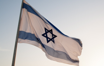 The Israeli flag with a Star of David waves against a clear sky.