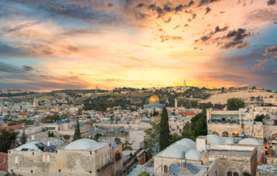 Sunset over Jerusalems old city, with the Dome of the Rock and a dramatic sky with clouds in the background.