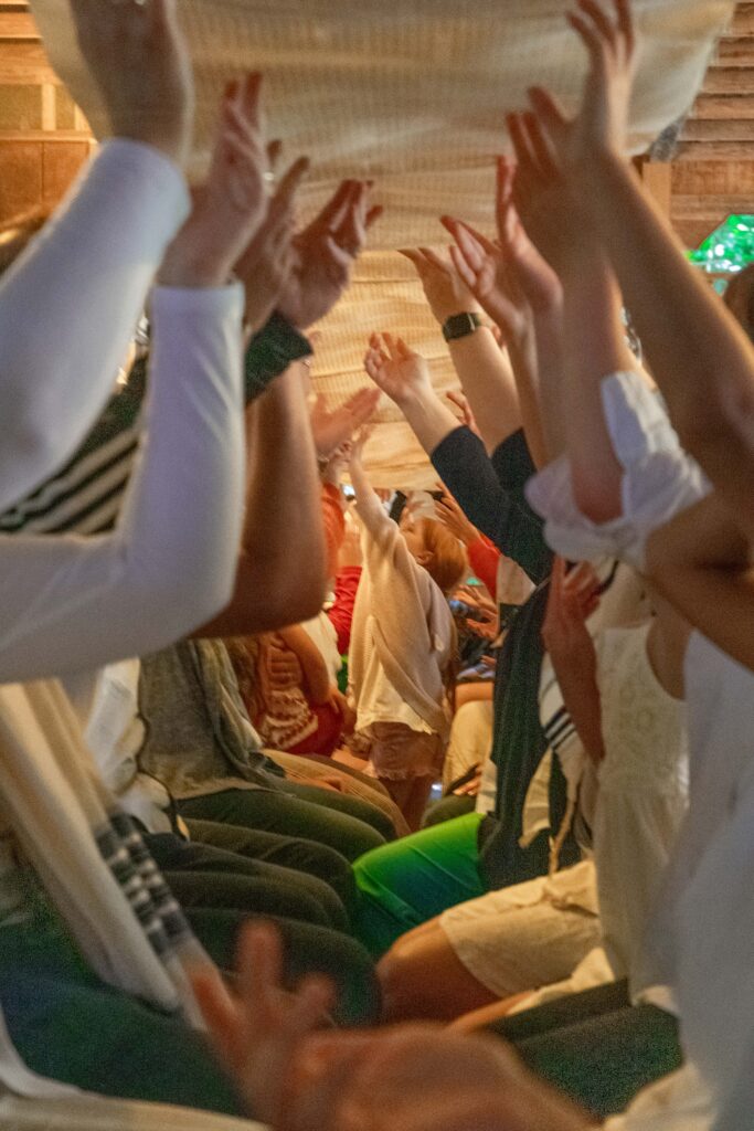 People raising their hands and forming a tunnel, while a child walks through it at a festive indoor event.