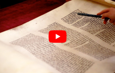 A person pointing at text on a scroll, with a red play button overlayed in the center.