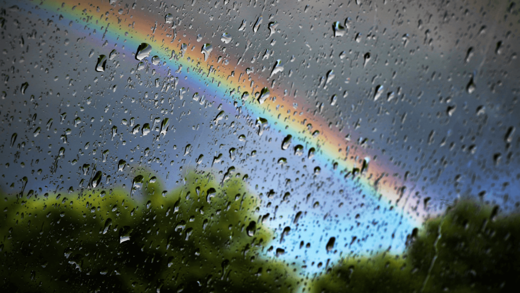 A rainbow viewed through a rainy window pane