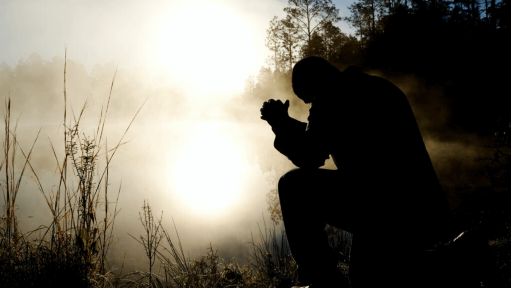 Silhouette of a person praying outdoors at dawn