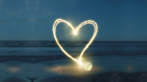 An illuminated, floating heart on a beach, with ocean water in the background. This image was to promote the recent Ritualwell program.