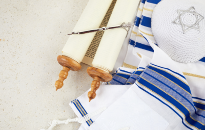 A Torah scroll, tallit, and kippah on a light background.