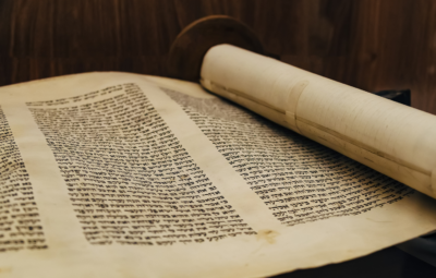 An open Torah scroll on a wooden surface, displaying Hebrew script on parchment.