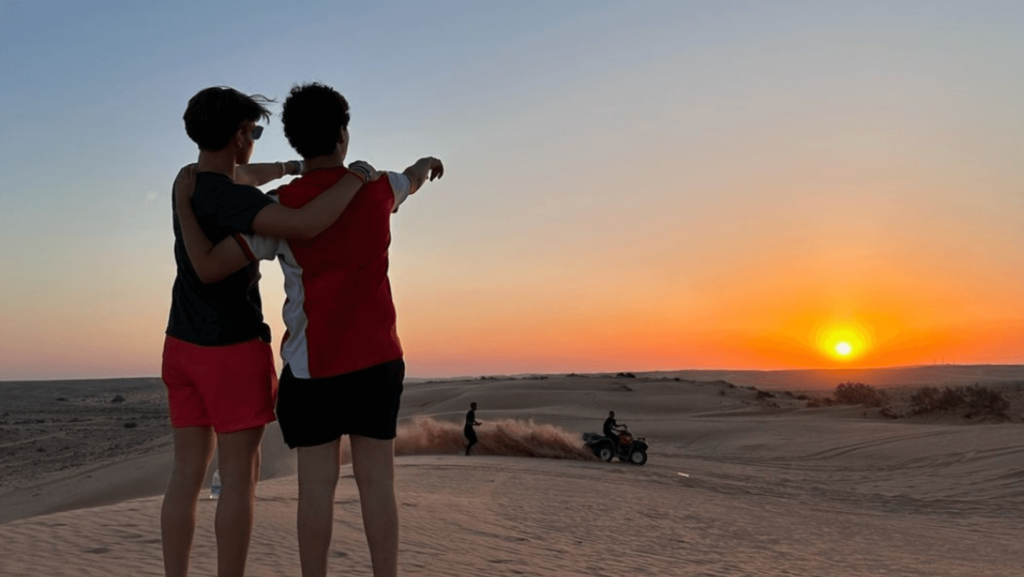 Two people on the beach pointing towards a sunset