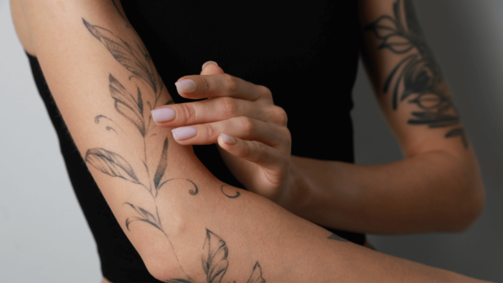 Person with floral and leaf tattoo designs on their arms in black ink