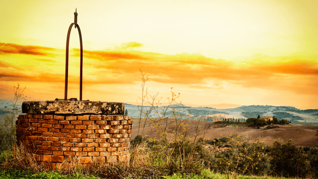 A stone well in a field at sunrise