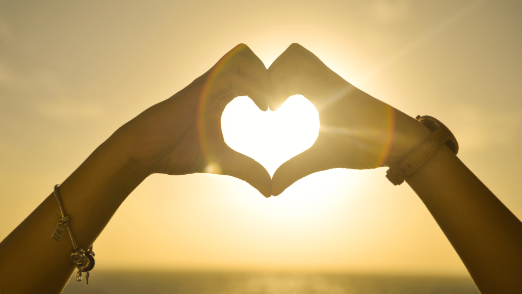 Person making a heart shape with their hands, backlit by the sun