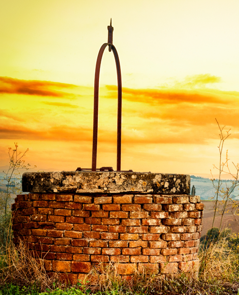 Old brick well with a metal handle under a vibrant orange sunset sky.