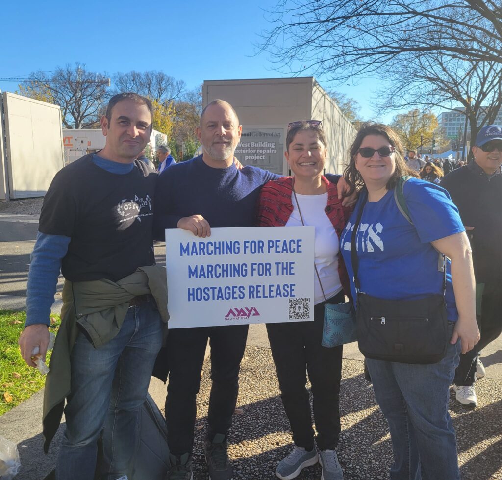 Four people holding a sign reading Marching for Peace, Marching for the Hostages Release at an outdoor event.