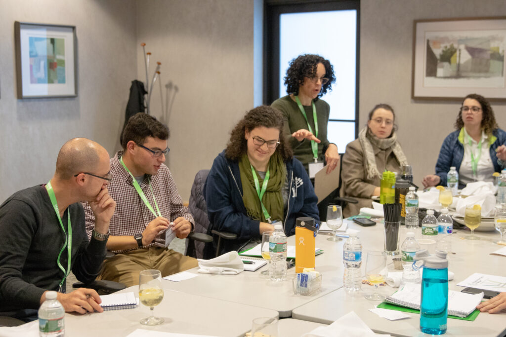 A group of people engaged in discussion around a conference table, with papers and drinks present.