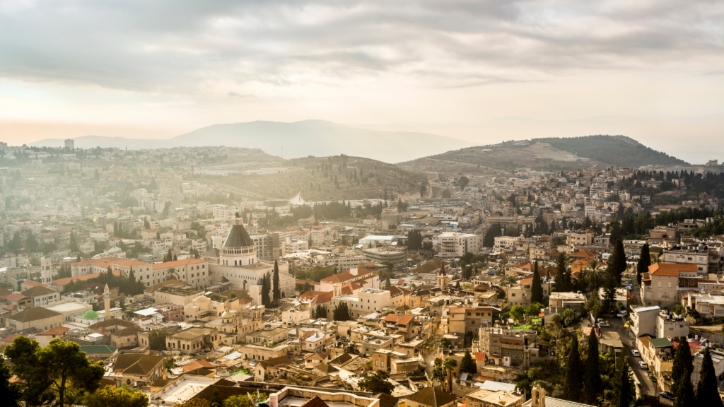 Aerial view of a city with densely packed buildings, mountains in the background, and a cloudy sky above.