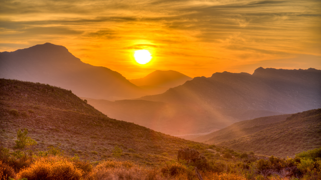 Sunset over a mountainous landscape with a glowing sky and silhouetted peaks.