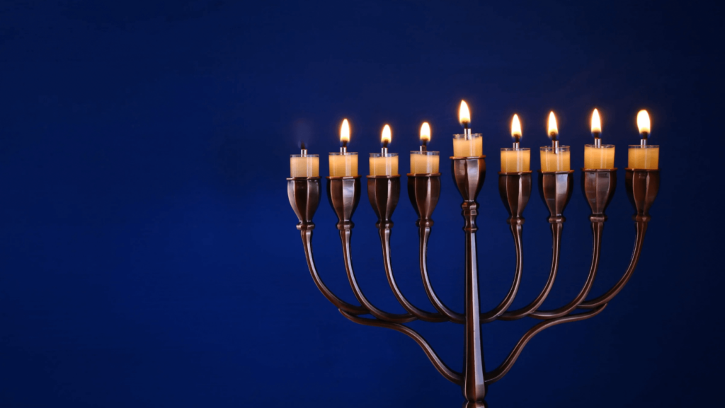 A metal menorah against a blue background with seven candles lit