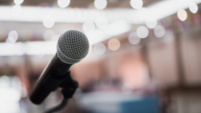 Close-up of a microphone on a stand with a blurred background of lights and soft colors.