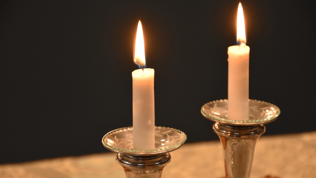 Two white candles, lit, in silver candlesticks
