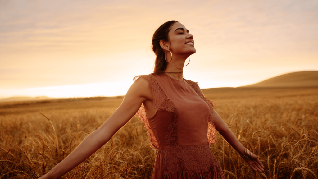 Woman with her eyes closed and her arms out smiling in the middle of a field