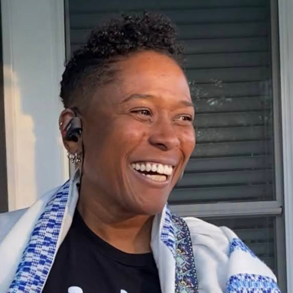 Wearing a tallit, Rabbi Sandra Lawson smiles. She appears to be outdoors on a front porch.