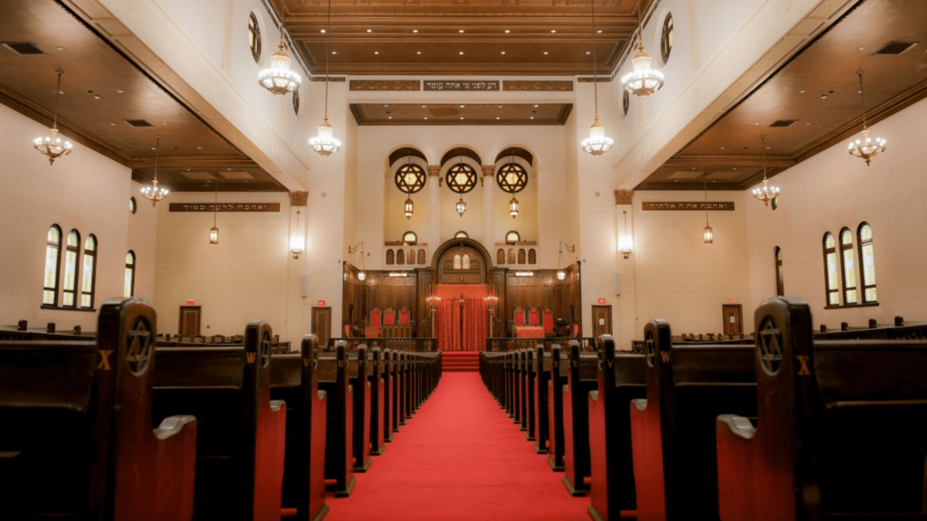 Interior of a synagogue sanctuary with a red carpet and dark wooden seats