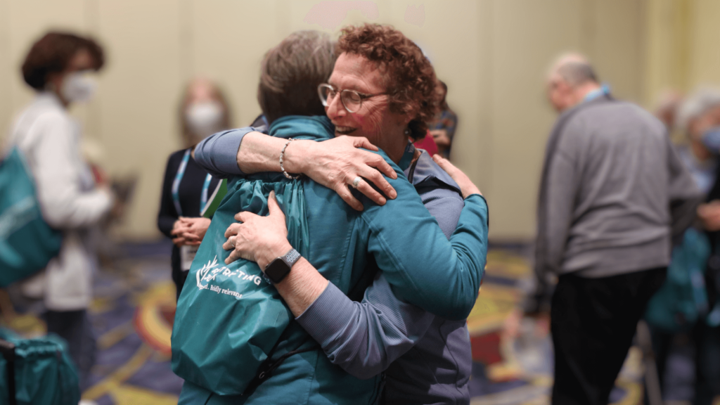 Two older people hugging, one wearing a Reconstructing Judaism backpack