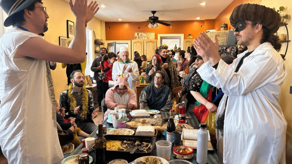 A large group of people in costume celebrating Purim at a table full of food