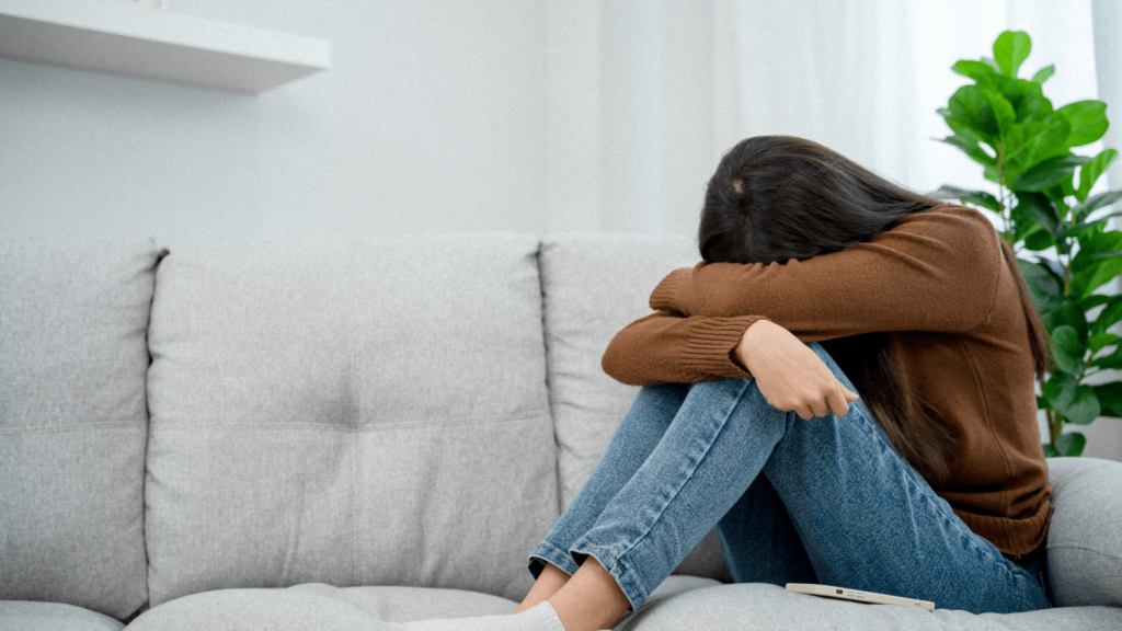 woman on a couch curled up with her head in her hands