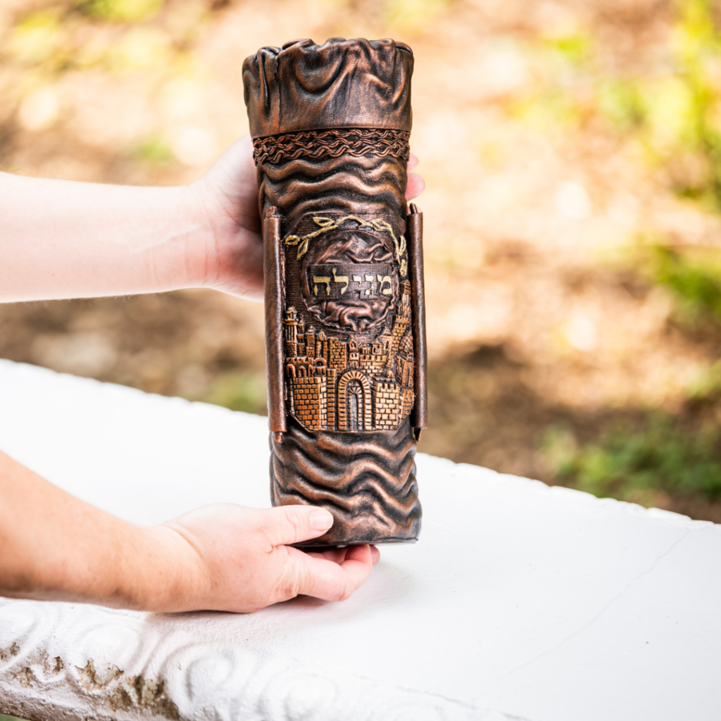 Hands holding a carved scroll case with intricate designs on a white surface outdoors.