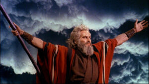 Charlton Heston as Moses, wearing his read cloak spreading his arms as the sky thunders.