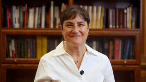 Person in a white shirt smiling in front of a wooden bookshelf filled with books.
