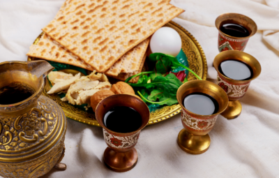 Passover Seder plate with matzah, egg, greens, and four cups of wine on a cloth background.