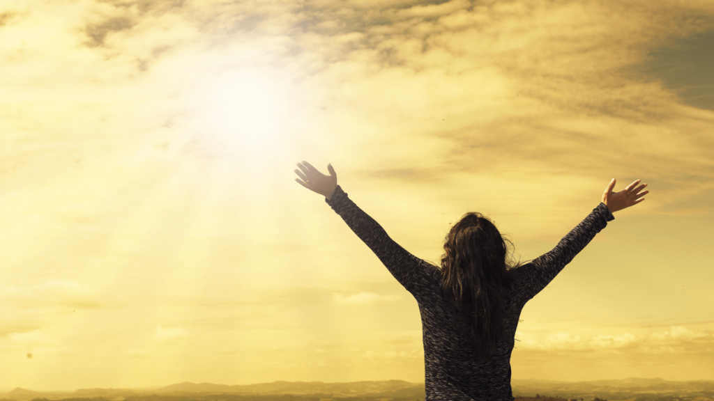 Person with their arms open against a sunny yellow sky